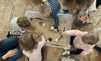 grupka dzieci bawiących się różnymi przedmiotami w piasku